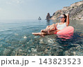 Woman vacation ocean woman in white swimsuit relaxing on pink inflatable ring in clear sea water near rocky cliffs on a sunny day 143823523