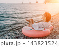 Woman, beach, ocean. Relaxing on a donut float on a pebble beach, enjoying summer vacation at sunset with copy space. 143823524
