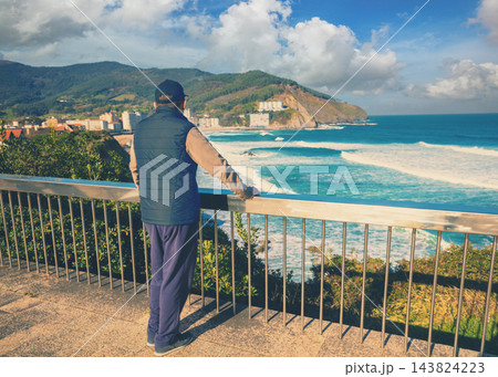 A man standing on the embankment and looking at the ocean and the beautiful bay. Bakio, Biscay, Basque Country, Spain, Europe A man standing on the embankment and looking at the ocean and the beautiful bay. Bakio, Biscay, Basque Country, Spain, Europe 143824223