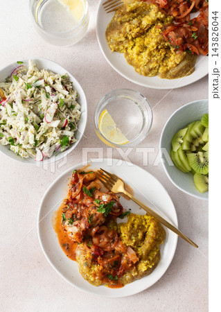 Plates hold amaranth, millet, and quinoa porridge served with baked white hake in tomato sauce. Fresh salad is beside the porridge. A bowl of kiwi sits nearby for dessert Plates hold amaranth, millet, and quinoa porridge served with baked white hake in tomato sauce. Fresh salad is beside the porridge. A bowl of kiwi sits nearby for dessert 143826044