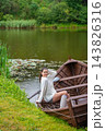 Young woman relaxing in wooden rowboat by lake on autumn day. Cozy sweater and rubber boots represent seasonal outdoor lifestyle and slow living in nature 143826316