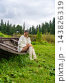 Young woman in white sweater and knee-high boots sits on an old wooden boat, surrounded by lush green grass and trees in a natural outdoor setting 143826319