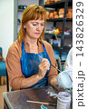 Woman over 50 painting handmade ceramic mug with brush in pottery workshop. Creative hobby represents active lifestyle and self expression in mature adulthood 143826329