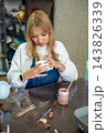Young woman smoothing glaze on handmade ceramic mug with finger after painting. Removing air bubbles and imperfections represents finishing process in pottery craft 143826339