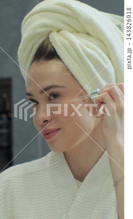 Woman applying facial serum using dropper standing in modern bathroom. Natural oil skin care morning routine. Facial skincare. 143826918