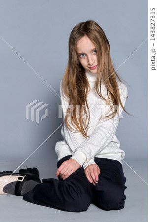 Thoughtful girl in textured sweater, perched casually chair. childhood elegance and relaxed attire. 143827315