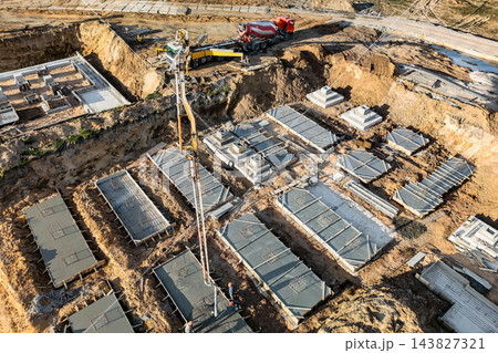Concrete foundation sections and trenches cover a building site, with an excavator and a red truck near the upper edge during daytime Concrete foundation sections and trenches cover a building site, with an excavator and a red truck near the upper edge during daytime 143827321