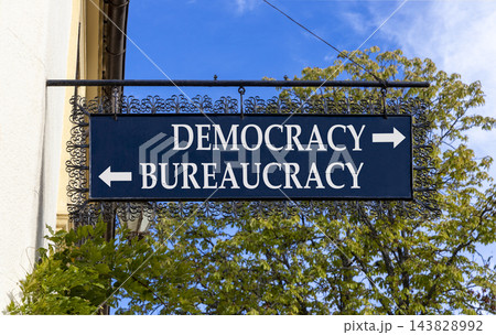 Democracy or bureaucracy words symbol. Concept words Democracy Bureaucracy on beautiful black road sign. Beautiful blue sky background. Business democracy bureaucracy concept. Copy space Democracy or bureaucracy words symbol. Concept words Democracy Bureaucracy on beautiful black road sign. Beautiful blue sky background. Business democracy bureaucracy concept. Copy space 143828992