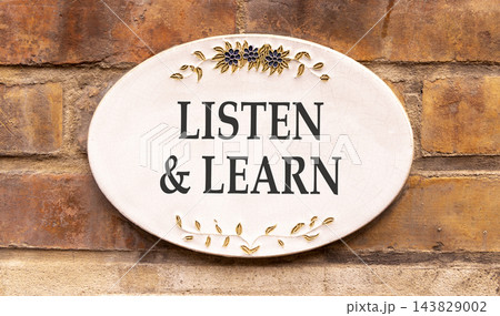 Listen and learn words symbol. Concept words Listen and learn on beautiful white sign plate. Beautiful brown brick wall background. Business listen and learn support concept. Copy space. 143829002