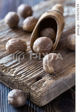 Whole nutmeg seeds scattered on rustic wooden surface with scoop Whole nutmeg seeds scattered on rustic wooden surface with scoop 143829234