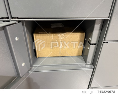 Cardboard package placed inside open gray parcel locker compartment with visible storage space 143829678