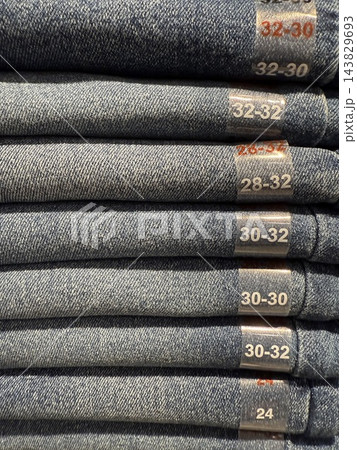 Stacked denim jeans with visible waist and length size labels in shades of blue and gray fabric 143829693