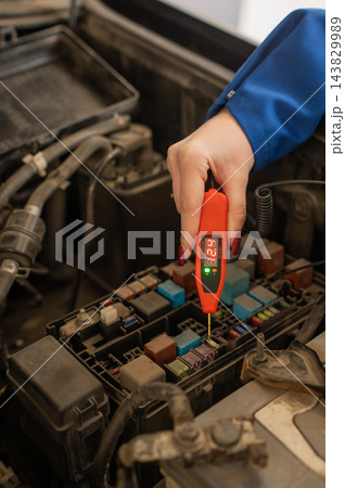 A mechanic checks a fuse in the car using a voltage tester. 143829989
