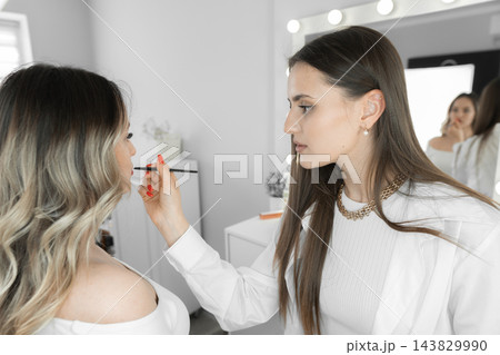 A skilled makeup artist works on a client's face, enhancing her features in a contemporary salon environment. The scene captures the artistry and precision involved in professional beauty services A skilled makeup artist works on a client's face, enhancing her features in a contemporary salon environment. The scene captures the artistry and precision involved in professional beauty services 143829990