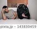 Humorous scene of puzzled young man looking at camera anonymous person sitting nearby with black trash bag over their head. Absurd concept concept of confusion, strange relationships, hiding. 143830459