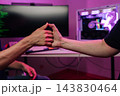 Close-up of male hands touching thumbs in friendly gesture. Modern tech background showing computer with code and gaming PC with purple neon lights. Concept of teamwork, success, gaming. 143830464
