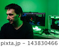 Focused young man, computer programmer or hacker, working at night. Dark room illuminated by green light from monitor, creating mysterious mood. Concept for cybersecurity, data breach, coding. 143830466