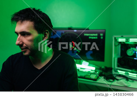 Focused young man, computer programmer or hacker, working at night. Dark room illuminated by green light from monitor, creating mysterious mood. Concept for cybersecurity, data breach, coding. Focused young man, computer programmer or hacker, working at night. Dark room illuminated by green light from monitor, creating mysterious mood. Concept for cybersecurity, data breach, coding. 143830466
