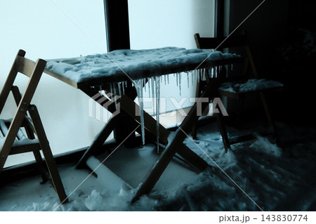 Wooden table and chairs covered in ice and snow near a bright window Wooden table and chairs covered in ice and snow near a bright window 143830774