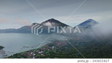 Batur caldera lake and surrounding villages resting peacefully at the base of Mount Batur and Mount Agung, partially obscured by low hanging mist and clouds on an overcast day 143831927