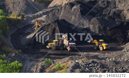 Construction vehicles wheel loaders and excavators moving and loading dark volcanic sand and rock into a dump truck, showcasing industrial mining operations in an open-pit quarry. Bali, Indonesia Construction vehicles wheel loaders and excavators moving and loading dark volcanic sand and rock into a dump truck, showcasing industrial mining operations in an open-pit quarry. Bali, Indonesia 143832272