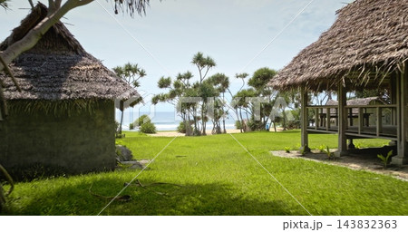 Traditional thatched roof bungalows on green grass meadow, tranquil tropical escape with serene white sand beach coast and the Pacific Ocean. Travel to Port Resolution, Tana Island exotic resort Traditional thatched roof bungalows on green grass meadow, tranquil tropical escape with serene white sand beach coast and the Pacific Ocean. Travel to Port Resolution, Tana Island exotic resort 143832363