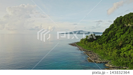 Tegua island landscape, part of the Torres islands in Vanuatu, features a rugged coastline with lush green tropical forest meeting the calm turquoise ocean under soft blue sky. Aerial drone flight Tegua island landscape, part of the Torres islands in Vanuatu, features a rugged coastline with lush green tropical forest meeting the calm turquoise ocean under soft blue sky. Aerial drone flight 143832364