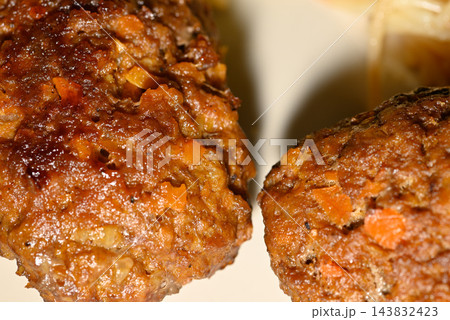 Two cooked meat patties with a dark brown crust and speckled orange carrot bits on a plain background 143832423