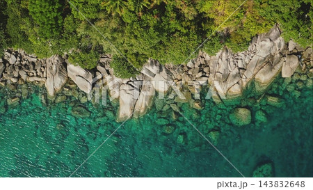 Turquoise ocean water gently splashing against a rocky coastline with lush green tropical vegetation framing the top of the scene in Phuket, Thailand. Natural background. Aerial top down view shot 143832648
