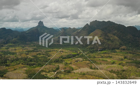 Khao Sok National Park panorama with lush rainforest, dramatic karst limestone peaks and patchwork cultivated valleys under an overcast sky, serene tropical wilderness scene. Aerial view drone flight 143832649