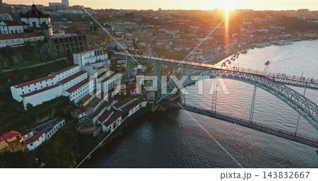 Aerial sunset view of Dom Luis I Bridge over Douro River, frame Porto and Vila Nova de Gaia with historic riverside architecture and port wine cellars reflecting warm evening light. Zoom out panorama Aerial sunset view of Dom Luis I Bridge over Douro River, frame Porto and Vila Nova de Gaia with historic riverside architecture and port wine cellars reflecting warm evening light. Zoom out panorama 143832667