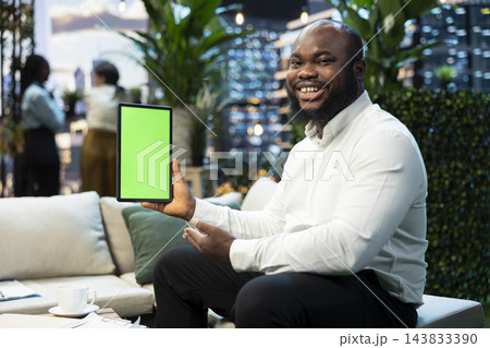Mockup tablet used by smiling businessman next to potted plants on rooftop terrace. Chroma key device used by cheerful man working on high rise skyscraper urban lounge Mockup tablet used by smiling businessman next to potted plants on rooftop terrace. Chroma key device used by cheerful man working on high rise skyscraper urban lounge 143833390