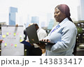 Businesswoman, laptop and typing as professional works while colleagues meet by strategy board. Productivity, digital workflow and coordination support flexible work on outdoor office terrace. 143833417