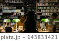Student, headphones and library anchor rear view of woman studying at shared table under green lamps. Independent learning, concentration and academic preparation unfold among books and classmates. 143833421