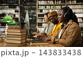 Student, headphones and keyboard draw focus as woman types on desktop computer in book-lined library. Digital learning, concentration and academic research support independent study at shared desk. 143833438