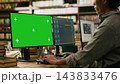 Green screen, monitor and computer mockup fill foreground while student types on keyboard in library. Screen replacement, digital learning and advertising offer editable desktop display context. 143833476