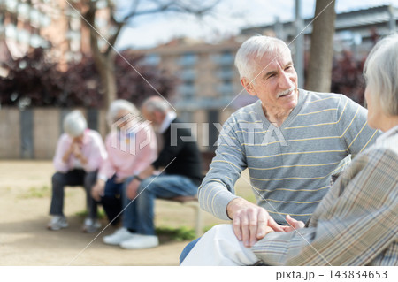 Elderly couple sitting on bench, flirting, chatting Elderly couple sitting on bench, flirting, chatting 143834653