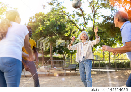 Joyful multiracial group of mature adult people playing volleyball game outdoors Joyful multiracial group of mature adult people playing volleyball game outdoors 143834686