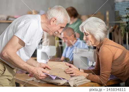 Elderly man and woman discussing pattern during sewing lesson Elderly man and woman discussing pattern during sewing lesson 143834811
