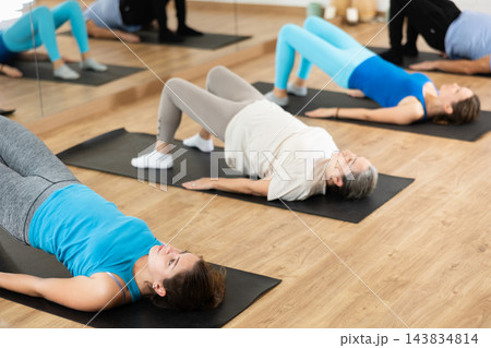People of different ages performing glute bridge during group Pilates workout. Active lifestyle and wellness concept People of different ages performing glute bridge during group Pilates workout. Active lifestyle and wellness concept 143834814