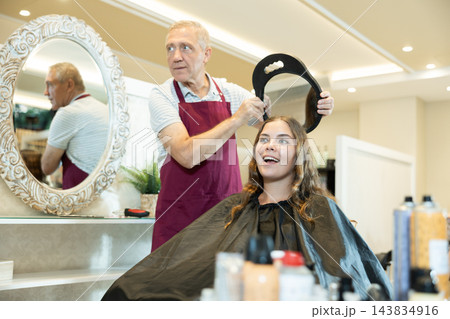 Experienced hairdresser showing result of hairstyling with mirror to happy girl 143834916
