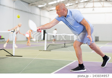 Mature man enjoying popular racket sport pickleball, playing doubles game with female friend on court Mature man enjoying popular racket sport pickleball, playing doubles game with female friend on court 143834957