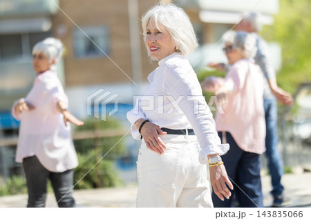 Group of elderly people doing arm swing exercises in courtyard Group of elderly people doing arm swing exercises in courtyard 143835066