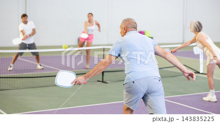 Rear view of elderly man playing pickleball on indoor court Rear view of elderly man playing pickleball on indoor court 143835225