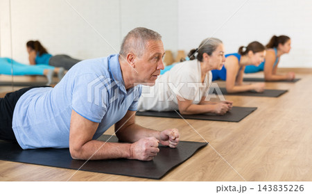 Senior man standing in plank pose in fitness studio Senior man standing in plank pose in fitness studio 143835226