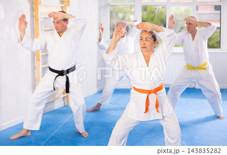 Old woman attendee of karate classes practicing kata standing in row with others 143835282