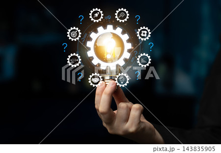 Hand Holding Light Bulb Surrounded by Gears and Question Marks Symbolizing Innovation, Ideas, Creativity, and Problem Solving Concepts in a Business Environment. Bitwise 143835905