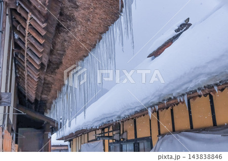 2月中旬の雪が降りしきる雪化粧した大内宿で茅葺屋根から垂れ下がるつららの列と民家を捉えた冬風景 2月中旬の雪が降りしきる雪化粧した大内宿で茅葺屋根から垂れ下がるつららの列と民家を捉えた冬風景 143838846