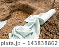 Gardening preparations are in progress with unrolled landscape fabric positioned next to a freshly dug hole, indicating a site ready for planting in sandy soil. 143838862
