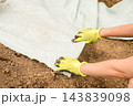 A worker is laying down protective fabric on prepared soil during a landscaping project. Hands wearing gloves carefully positioning the fabric for effective drainage management. 143839098